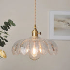 The Clérachic Scalloped Flower Glass Pendant Light in clear ribbed glass, hung beside framed art and a eucalyptus sprig in a calm room.