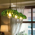 Three Clérachic Scalloped Flower Glass Pendant Lights in green glass hung in a row beside a curtained window in a living room.