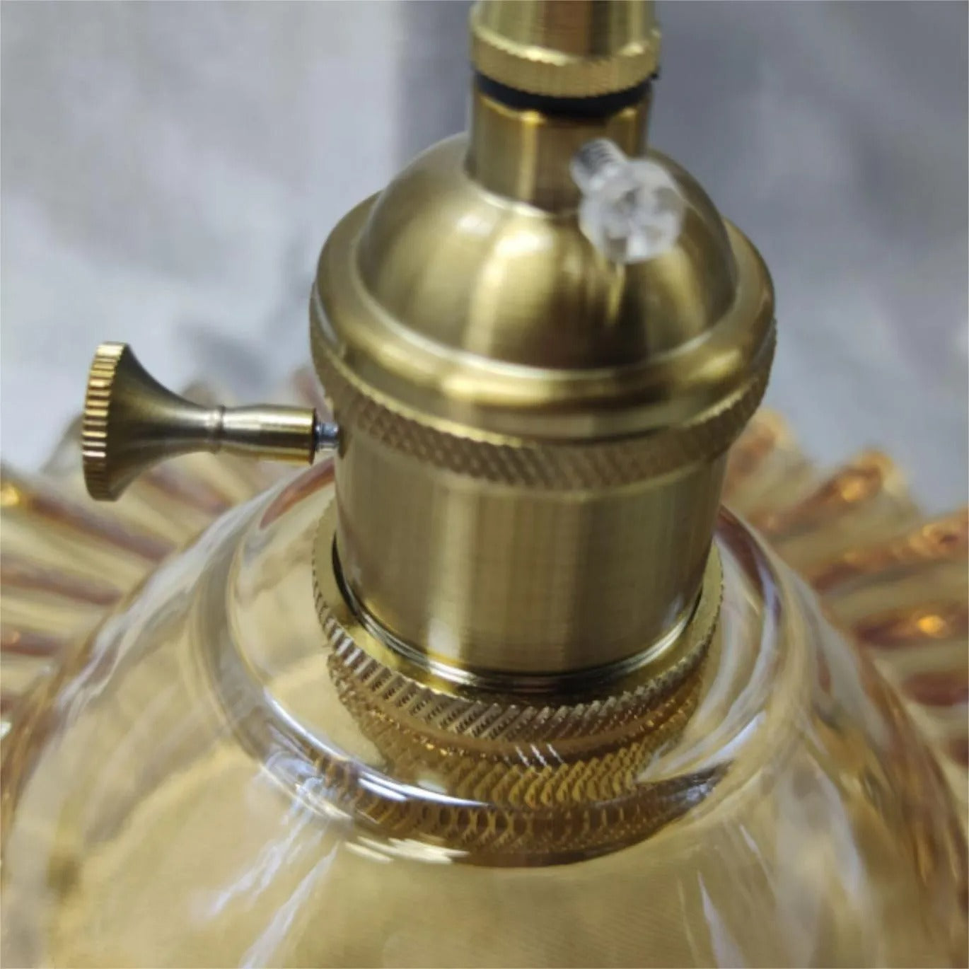 Close-up of the Clérachic Scalloped Flower Glass Pendant Light's knurled brass socket and on/off turn knob above the amber glass.