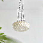 The unlit ivory Clérachic scalloped glass dome pendant light against a white wall, a houseplant blurred in the foreground