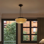 A beige Clérachic scalloped glass dome pendant light lit in a living room beside a black-framed window and brick courtyard
