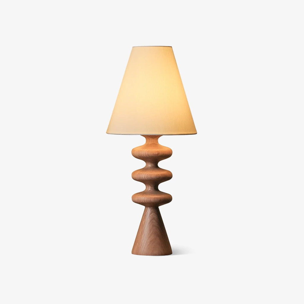 Wood-tone Clérachic table lamp with a white fabric shade, a stacked, rippled turned base and a cone foot, on a plain light backdrop.