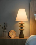 Lit Clérachic table lamp on a bedside shelf next to a round wooden clock, its rippled base in a warm brown tone.