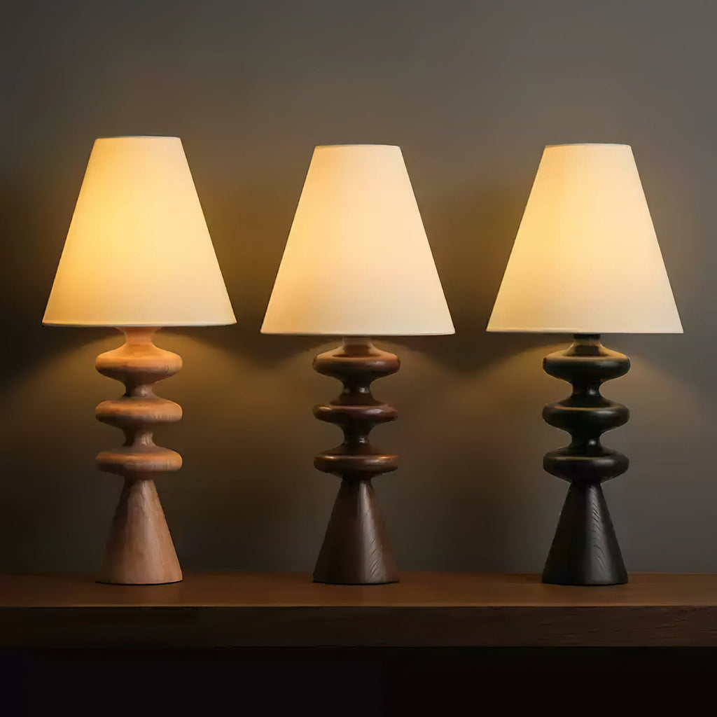 Three Clérachic table lamps in a row on a dark shelf, their rippled bases in wood tone, walnut and black, all with lit white shades.