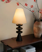 Black Clérachic table lamp on a dark wooden console, with a terracotta vase and bare red-berried branches beside it.