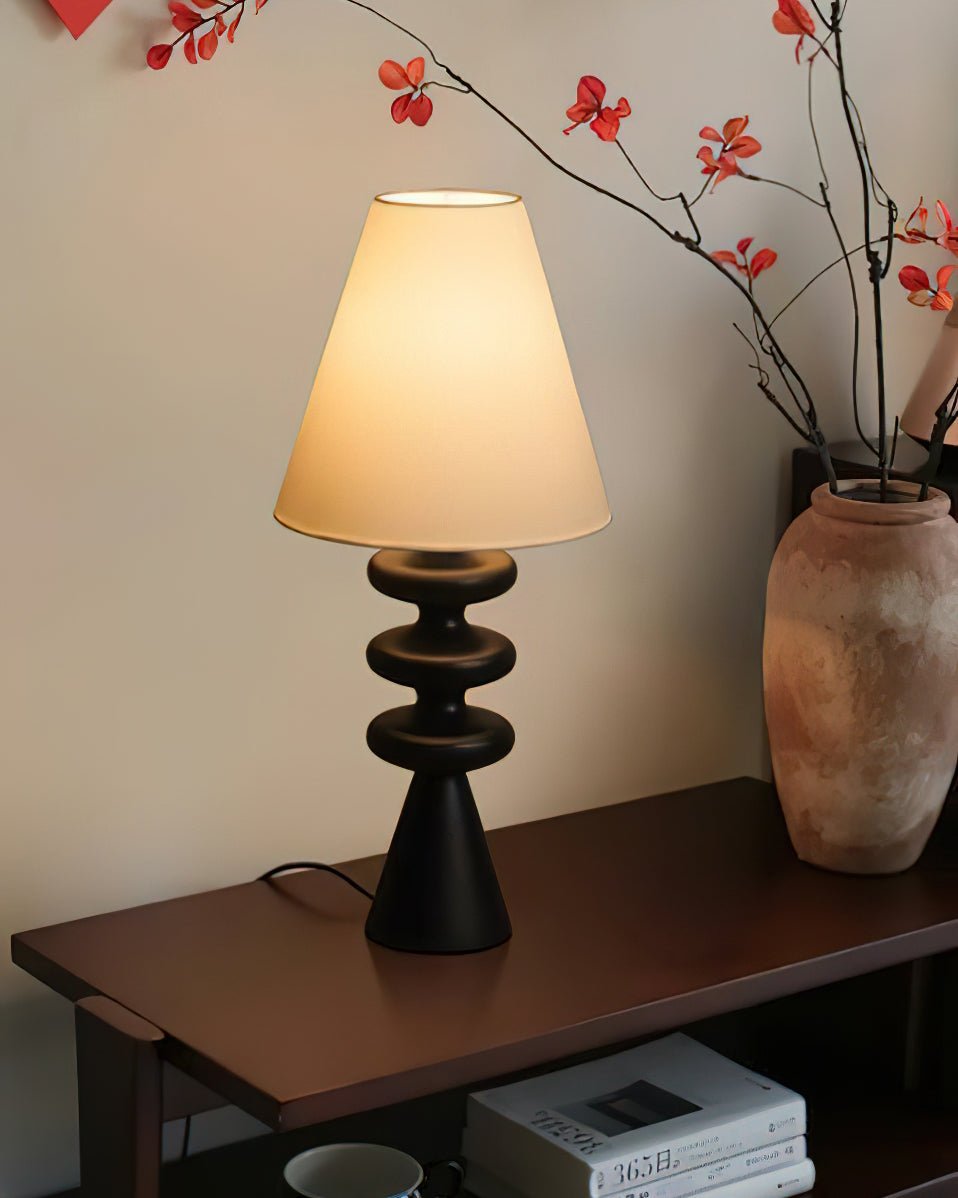 Black Clérachic table lamp on a dark wooden console, with a terracotta vase and bare red-berried branches beside it.