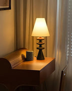 Warmly lit Clérachic table lamp on a small roll-top desk beside a patterned mug, with draped curtains behind.