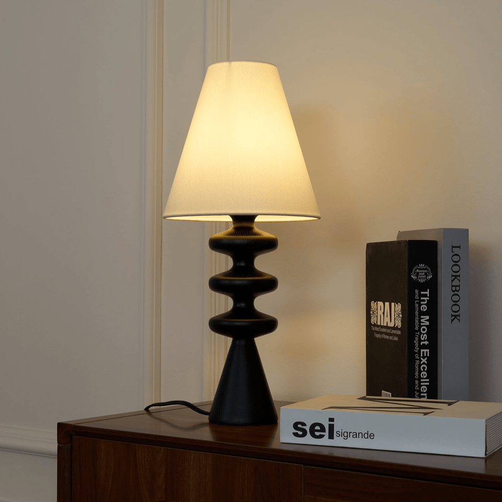 Black Clérachic table lamp on a walnut sideboard in front of panelled walls, with art books stacked beside it.