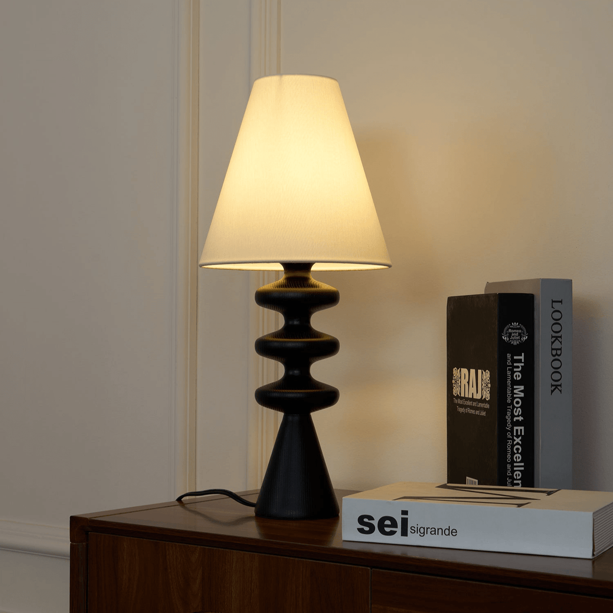 Black Clérachic table lamp on a walnut sideboard in front of panelled walls, with art books stacked beside it.