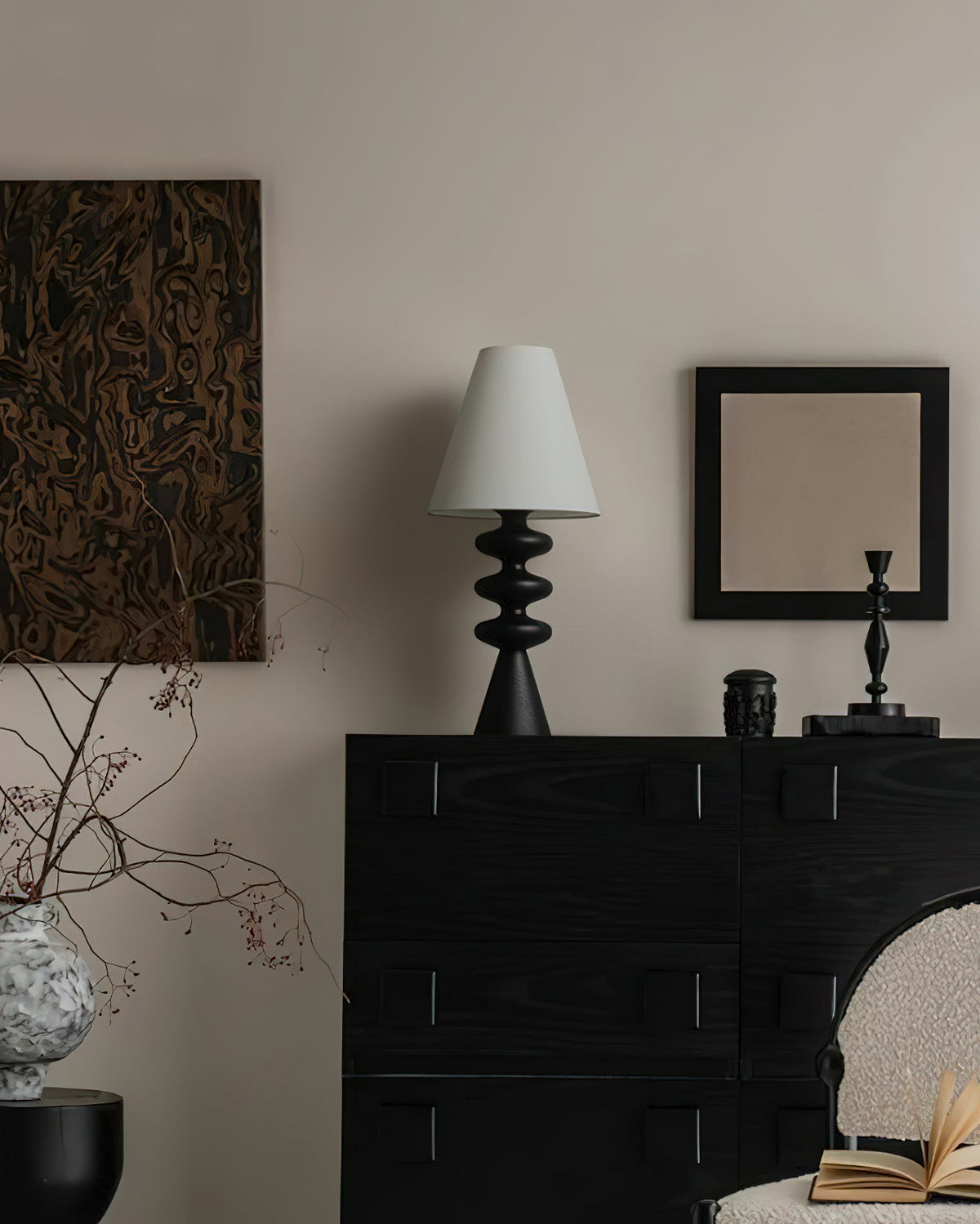 Unlit black Clérachic table lamp with a pale shade on a black chest of drawers in a room with a framed mirror and dark artwork.