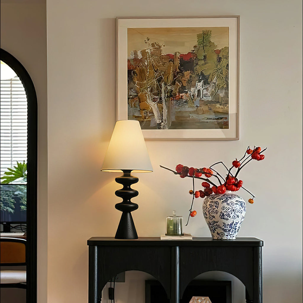 Clérachic table lamp lit on a black console table, beside a blue-and-white vase of berry branches under a painted landscape.