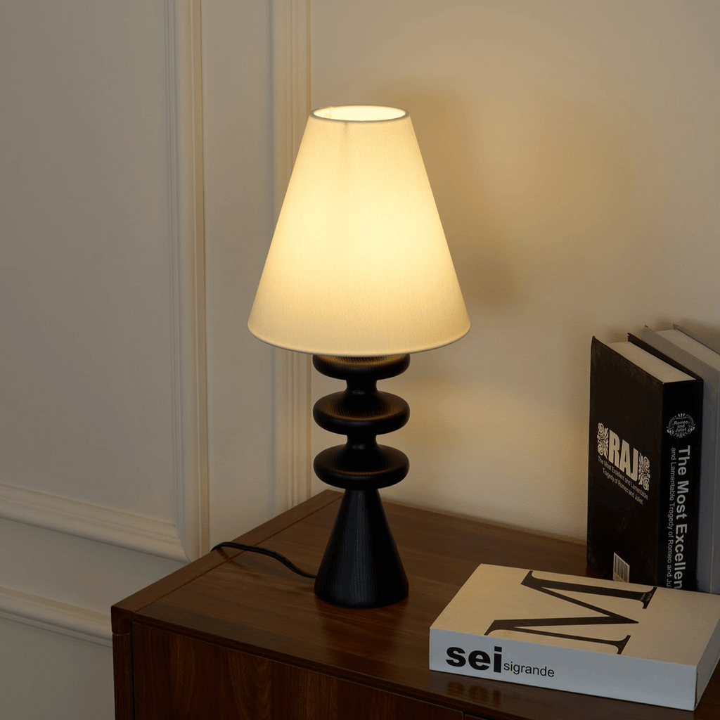Black Clérachic table lamp on a walnut cabinet, photographed from above, with a pile of art books at its side.