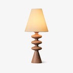 Wood-tone Clérachic table lamp glowing on a pale grey backdrop, its rippled turned base and cone foot casting a soft shadow.