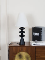 Unlit white fabric shade on a black Clérachic table lamp, standing on a walnut sideboard with a cane panel against a white wall.