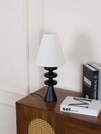 Black Clérachic table lamp with an unlit white shade, set at a slight angle on a walnut cabinet beside a stack of books.