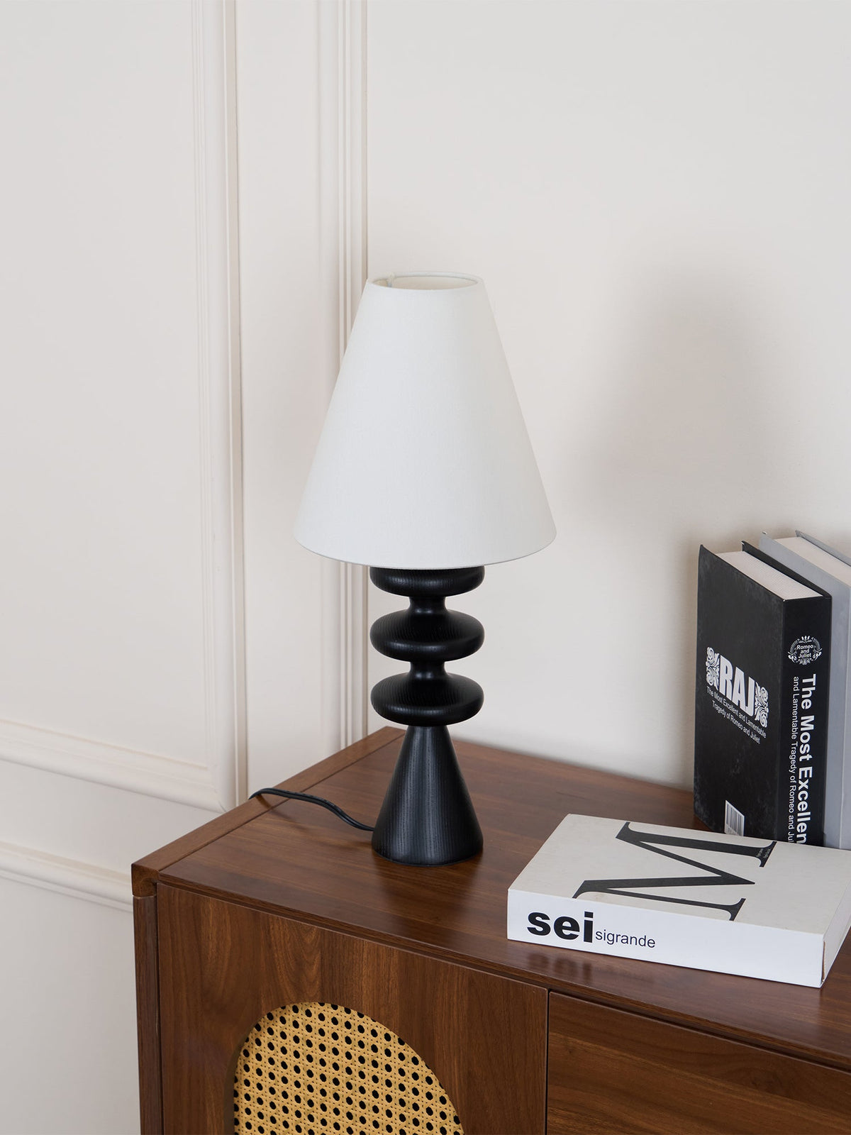 Black Clérachic table lamp with an unlit white shade, set at a slight angle on a walnut cabinet beside a stack of books.