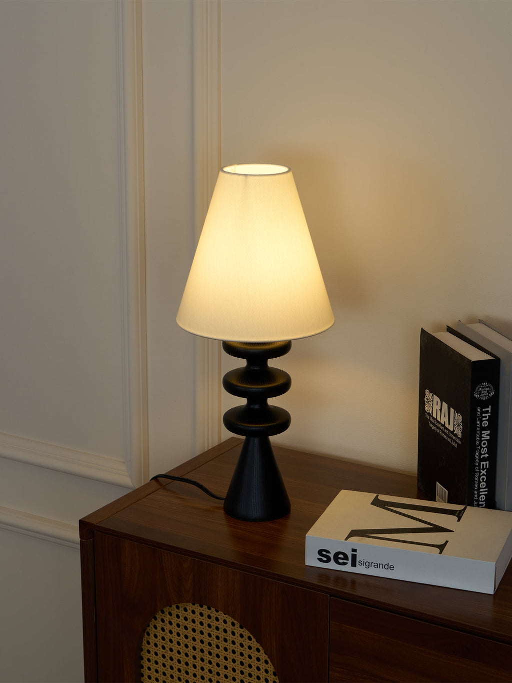 Clérachic table lamp lit brightly on a walnut cabinet, its black rippled base standing out against a warm grey wall.