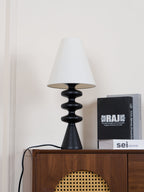 Black Clérachic table lamp on a cabinet seen from low down, its white shade unlit and a black cord trailing to the left.