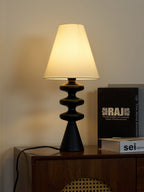 Black Clérachic table lamp glowing on a walnut cabinet from a slightly raised angle, with dark books beside it.