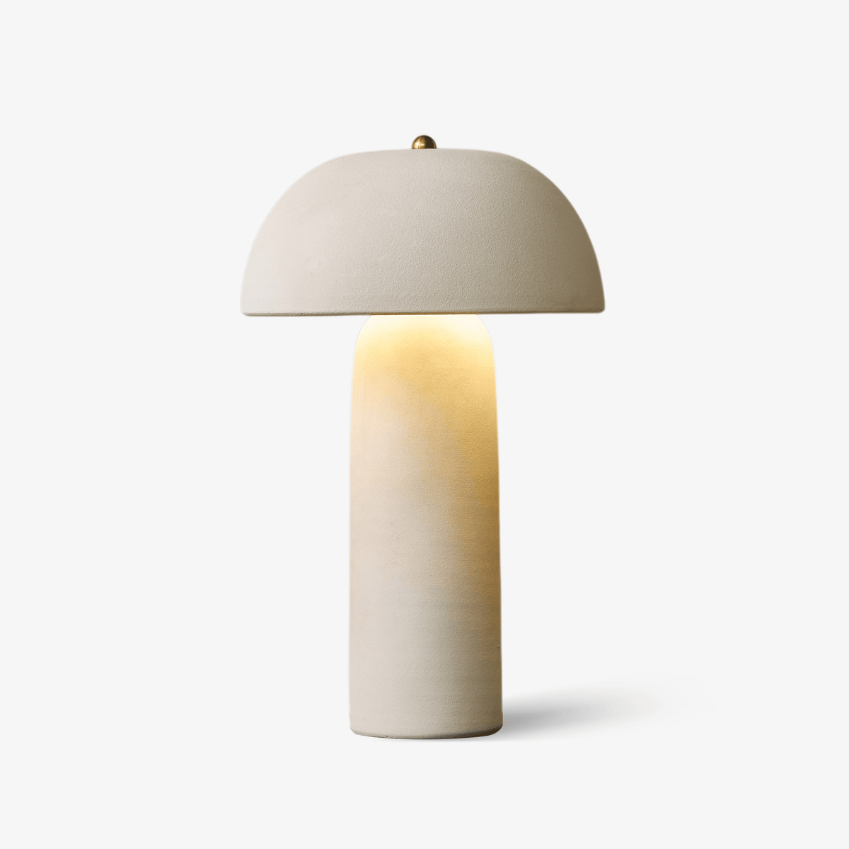 Ceramic table lamp with a domed cream shade, a brass finial and a slim rounded column that glows from within, on a pale backdrop; a Clérachic lamp.