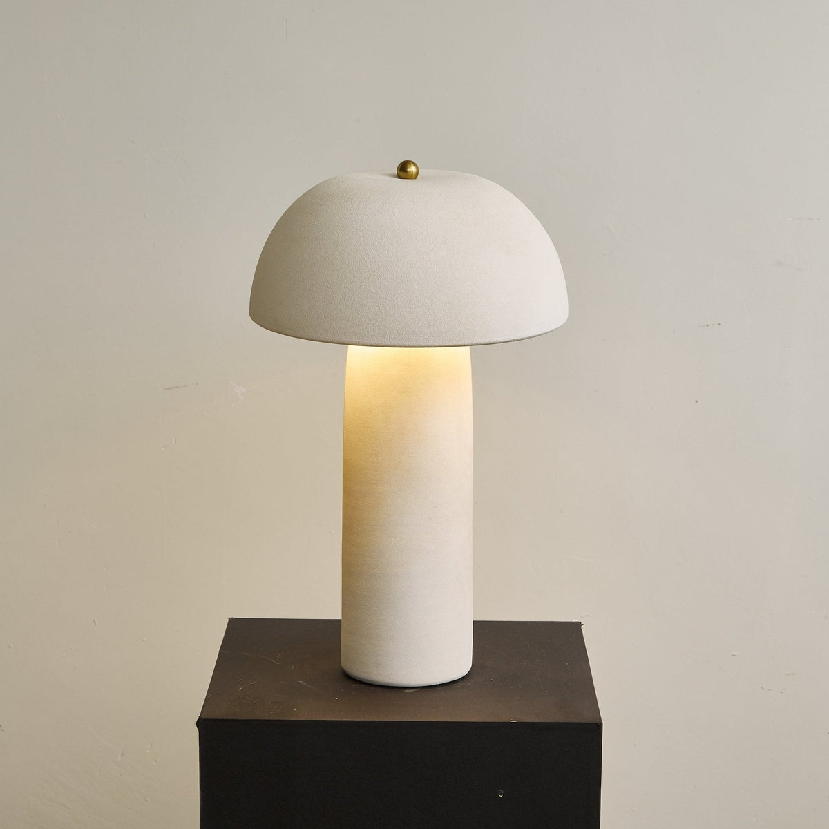 Lamp shown from further back on a dark plinth, with the light glowing up from the base of the dome; a Clérachic table lamp.