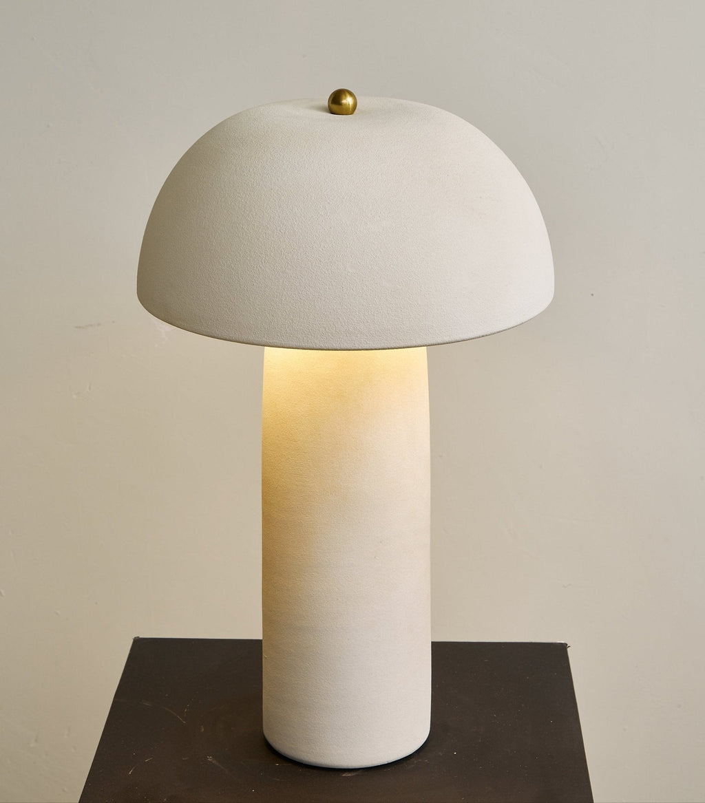 Tight crop of the dome, the brass finial and the lit column, with a dark plinth below; a Clérachic table lamp.