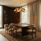 The Clérachic gold sculptural chandelier lit above a long dining table with upholstered chairs and paneled walls.