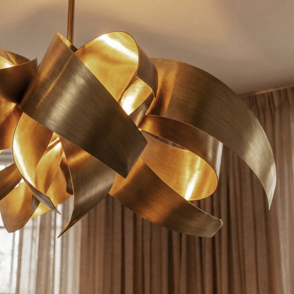 Close detail of the Clérachic gold sculptural chandelier, showing the brushed texture and curve of its steel ribbons.