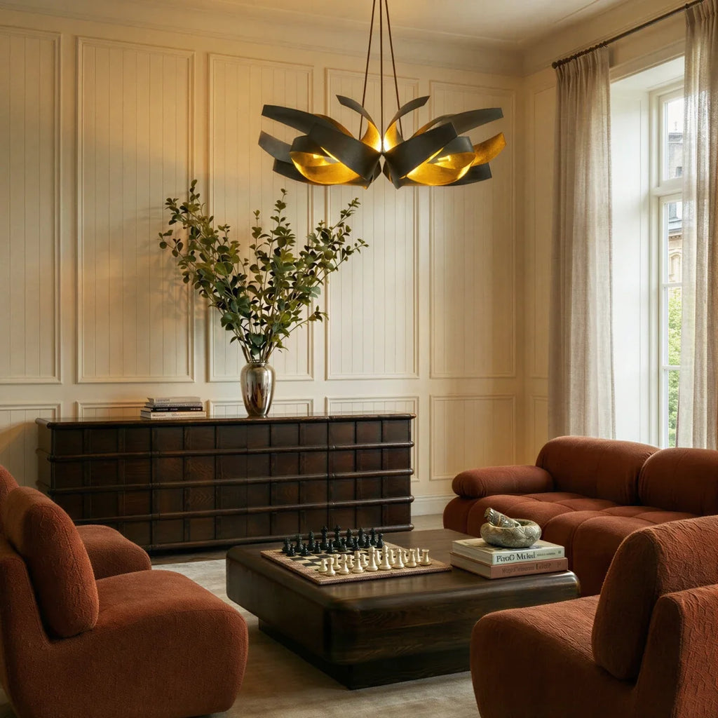 The Clérachic black and gold sculptural chandelier lit above a living room with terracotta sofas and a chess set.