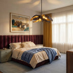 The Clérachic black and gold sculptural chandelier lit above a bed with a maroon velvet headboard and gold curtains.