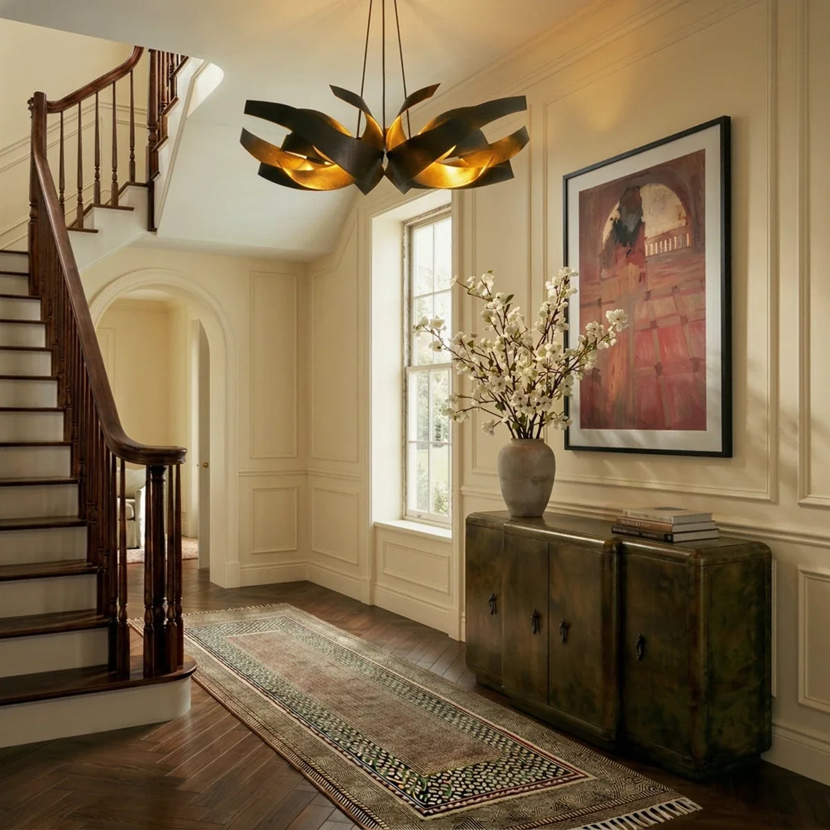 The Clérachic black and gold sculptural chandelier lit above a staircase landing with a runner rug and framed art.