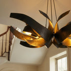 Close detail of the Clérachic black and gold sculptural chandelier, its steel ribbons spread wide above a staircase.