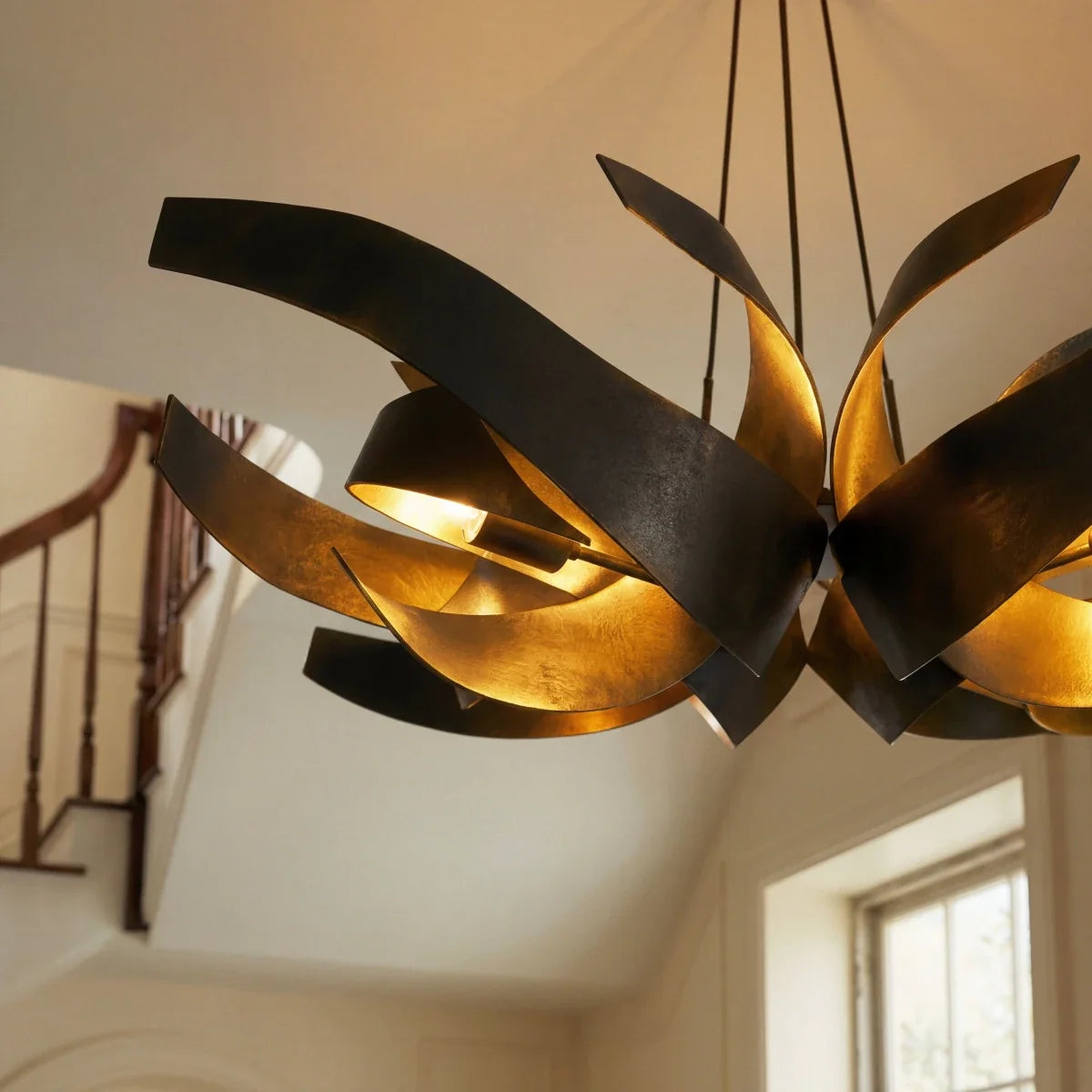 Close detail of the Clérachic black and gold sculptural chandelier, its steel ribbons spread wide above a staircase.