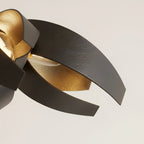 Close view of two overlapping steel ribbons, the hammered black outer face curling past the brushed gold inner face where the light catches it