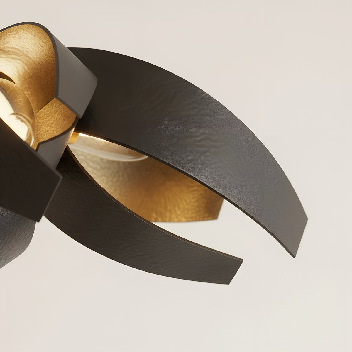 Close view of two overlapping steel ribbons, the hammered black outer face curling past the brushed gold inner face where the light catches it