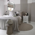 Small black Clérachic table lamp on a white bedside chest in a grey bedroom with a round mirror, a striped panel and a woven rug.