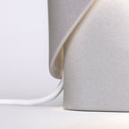 Close view of the fold where the shade meets the cone base on this Clérachic table lamp in grey, with a white cord below.