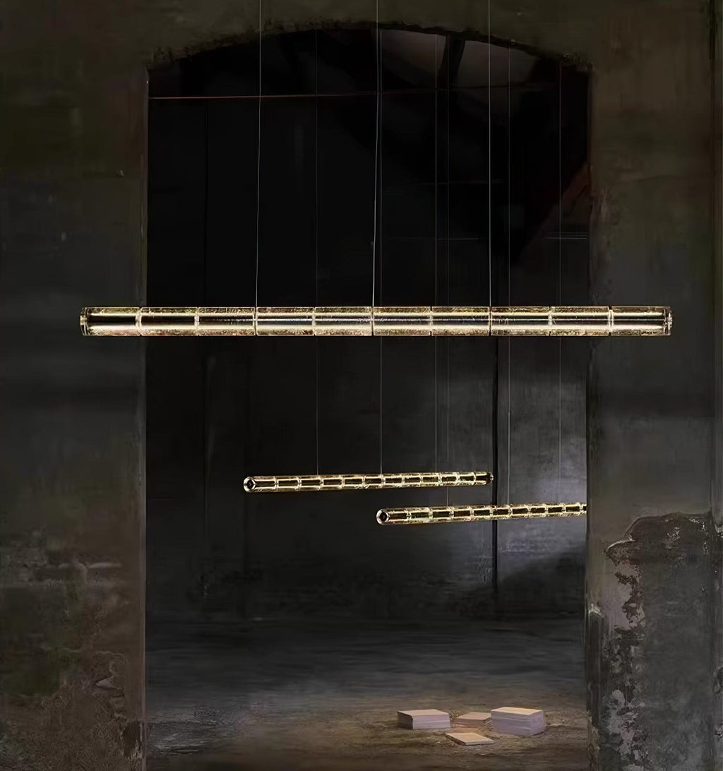 Three Clérachic segmented glass chandeliers hung at different heights in a dark arched concrete space, lit warm along their length.