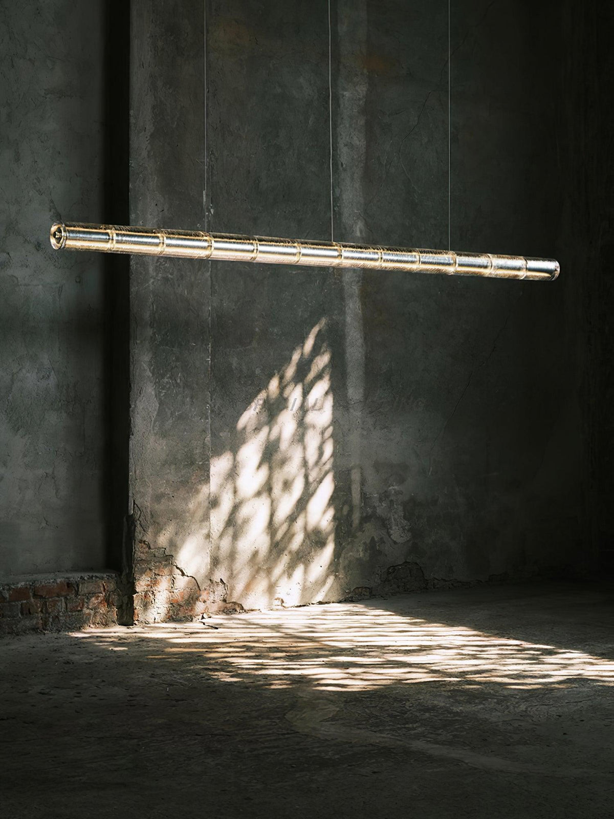 Lit segmented glass chandelier from Clérachic hanging in a bare concrete room, with dappled sunlight falling on the floor beneath.