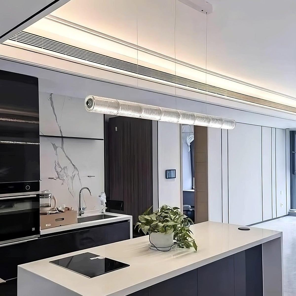 This Clérachic linear chandelier hangs above a white kitchen island, its clear glass segments glowing against a marble-clad wall.