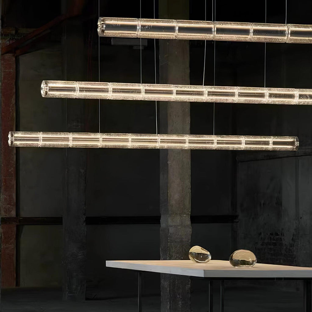 Three lit glass-segment chandeliers from Clérachic stacked at staggered heights over a pale table with two glass pebbles on it.