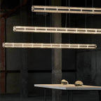 Three lit glass-segment chandeliers from Clérachic stacked at staggered heights over a pale table with two glass pebbles on it.