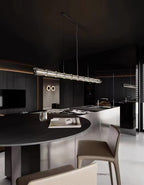 A Clérachic glass-segment chandelier lit over a round dark dining table in a moody kitchen with leather-seated stools.
