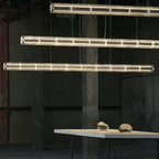 Three Clérachic segmented glass chandeliers glowing warm in a raw industrial hall, with a white table and glass pebbles below.