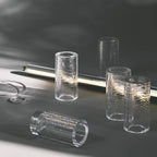 Chunks of crackle-textured clear glass cylinders on a grey surface beside a glowing tube, showing the glass used in this Clérachic chandelier.