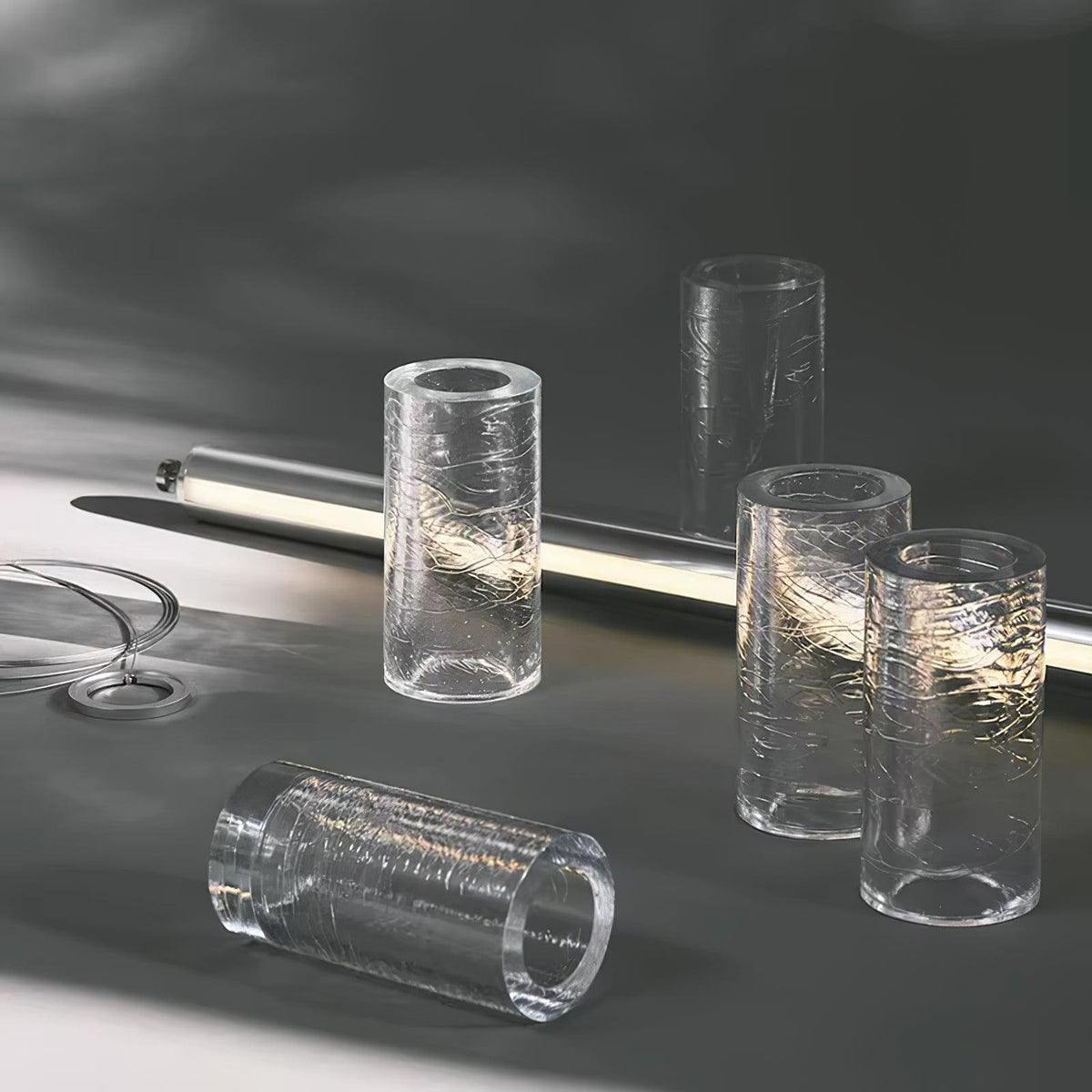 Chunks of crackle-textured clear glass cylinders on a grey surface beside a glowing tube, showing the glass used in this Clérachic chandelier.