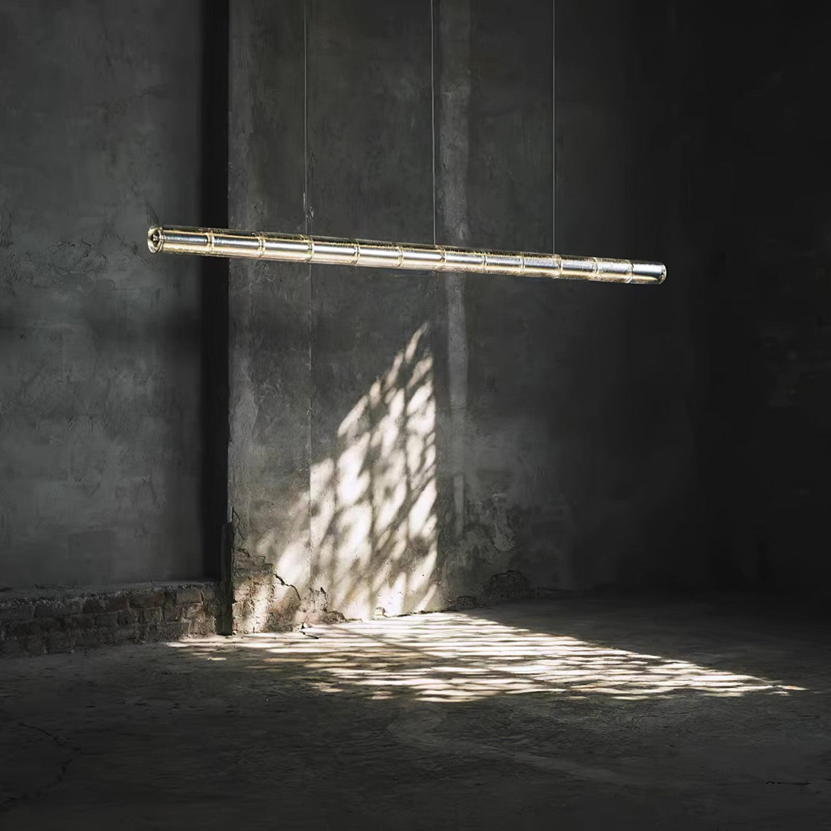 Single lit Clérachic glass chandelier suspended in a dim concrete room, with a pattern of light on the wall and floor.