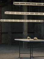 Portrait view of three tiers of this Clérachic segmented glass chandelier above a long table on black metal legs.