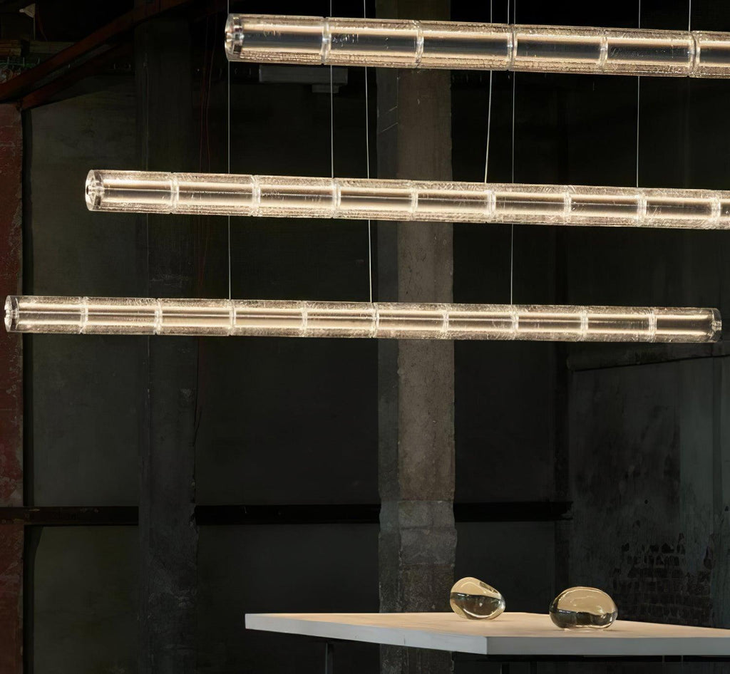 Three lit rows of segmented clear glass from Clérachic hang in an industrial space, with a table and glass pebbles at the bottom.