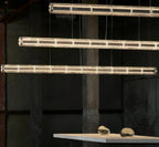 Three lit rows of segmented clear glass from Clérachic hang in an industrial space, with a table and glass pebbles at the bottom.